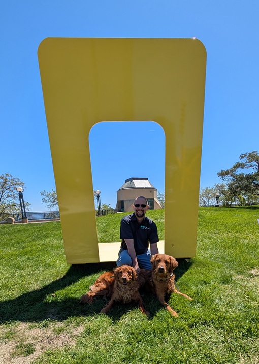 Dog trainer Jacob with two golden retrievers holding a down in front of Michelle Grabner's Untitled (Yellow) on a clear day full of sunshine.